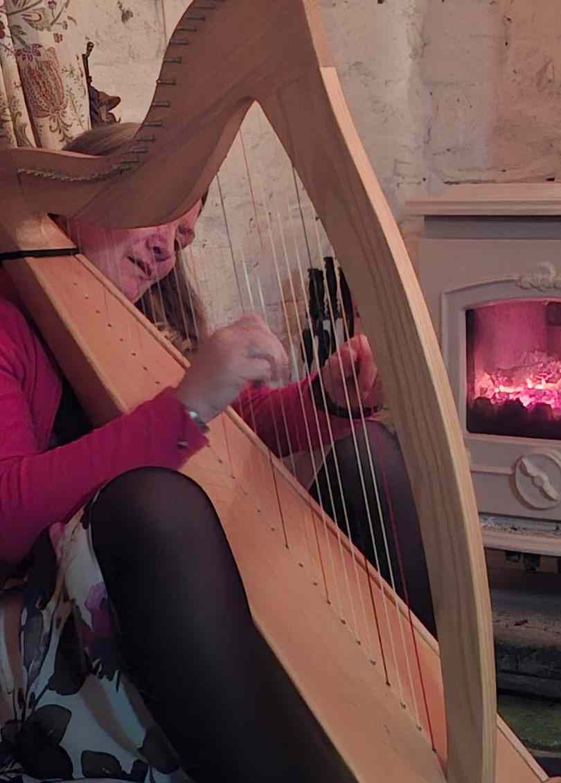 A lady playing a small harp near a stove. The photo is set in an old stone building